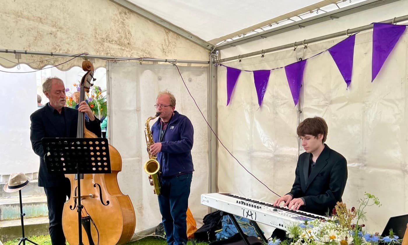Blue Sky Music trio playing double bass, saxophone and keyboard in a marquee with purple bunting