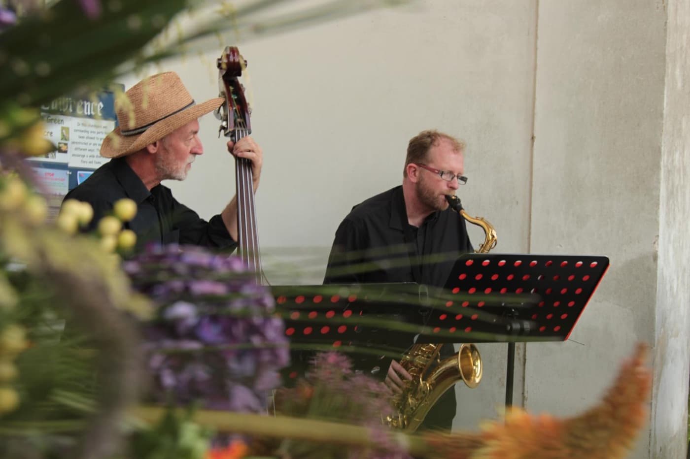 Saxophone and double bass duo playing outdoors behind summer flowers