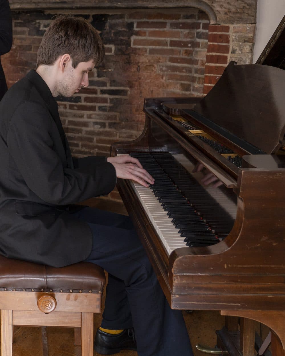 Tom playing a grand piano in front of a brick fireplace